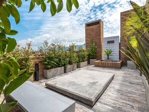 A rooftop patio with a concrete floor, wooden planters, and a brick wall.