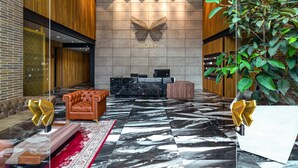 Eine moderne Lobby mit einer Rezeption, Ledersitzgelegenheiten, einem großen Spiegel und einem Wandkunstwerk.