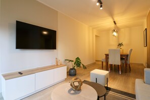 A modern living room with a flat-screen TV mounted on the wall, a dining area with a table and chairs, and a seating area with ottomans. - w Breathtaking 2BR With Balcony in Miraflores (Lima)