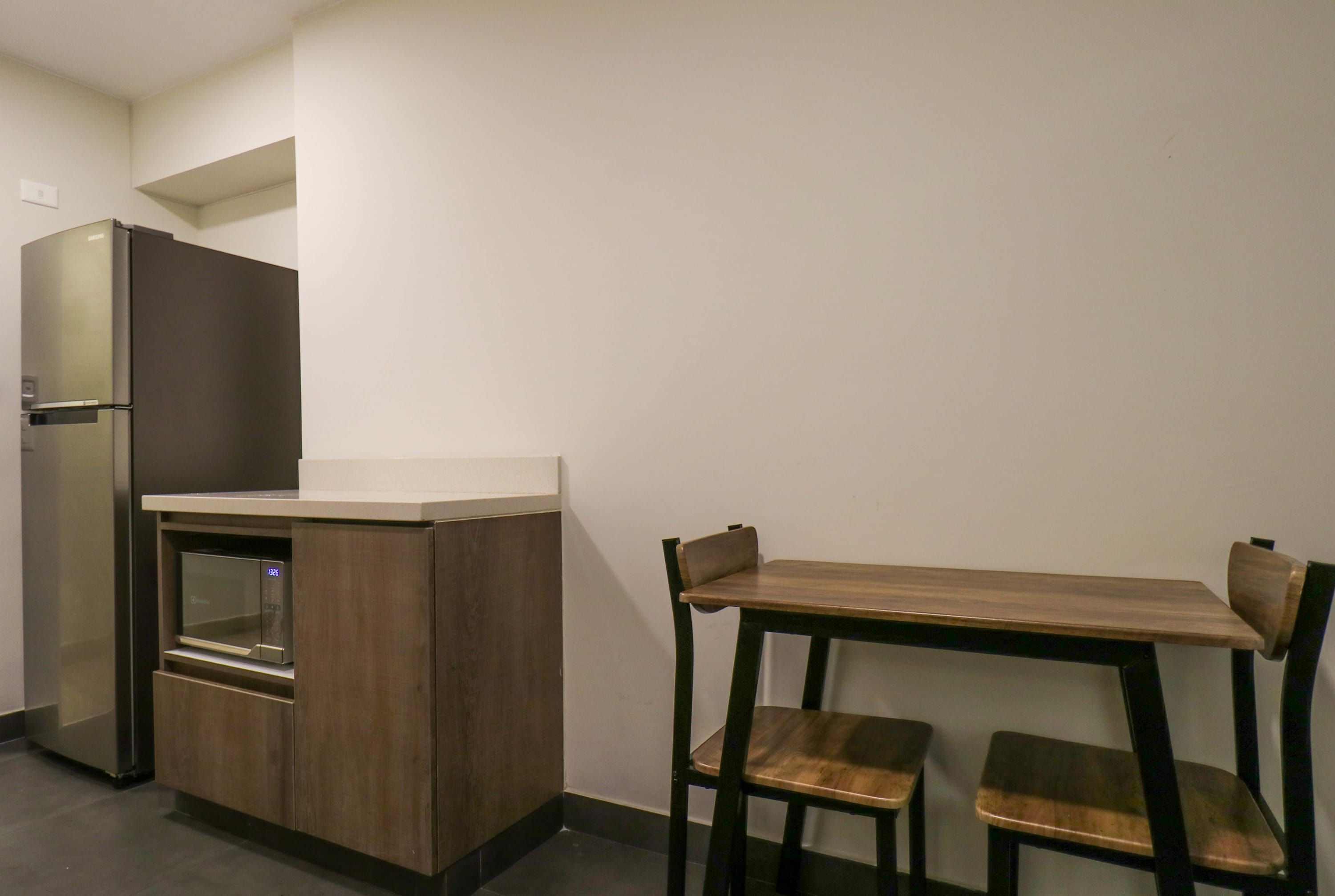 A compact kitchenette with a refrigerator, microwave, and oven, and a small dining table with two chairs.