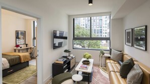 Ein modernes Wohnzimmer mit einer Couch, einem Couchtisch, einem Fernseher und einem großen Fenster mit Blick auf die Stadt.
