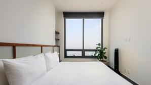 A hotel room with a large bed, a window with a city view, a plant, and a black device on the nightstand. - w Luxurious 1BR w/ Amazing View in Cuauhtémoc (Mexico City)