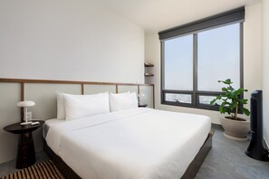 A hotel room with a large bed, a nightstand, a potted plant, a window with a view, and a standing fan. - w Luxurious 1BR w/ Amazing View in Cuauhtémoc (Mexico City)