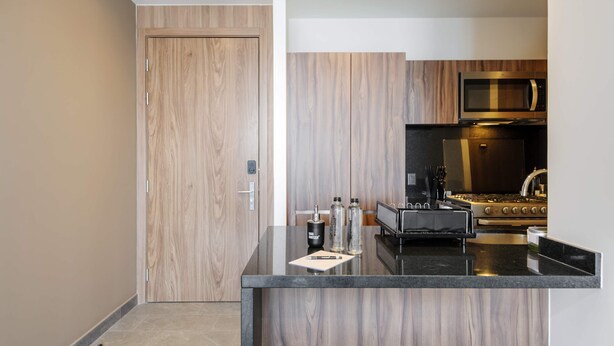 A modern kitchen with a wooden door, a black countertop, and stainless steel appliances. - w Luxurious 1BR w/ Amazing View in Cuauhtémoc (Mexico City)