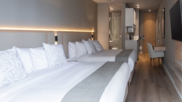 A modern hotel room with two beds, a desk, and a shower area.