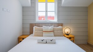 A bedroom with a large bed, a window with a view, a bedside table with a lamp, and a headboard.