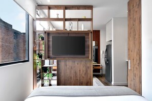 A modern bedroom with a large bed, a TV mounted on a wooden panel, and a view of a cityscape through a window.