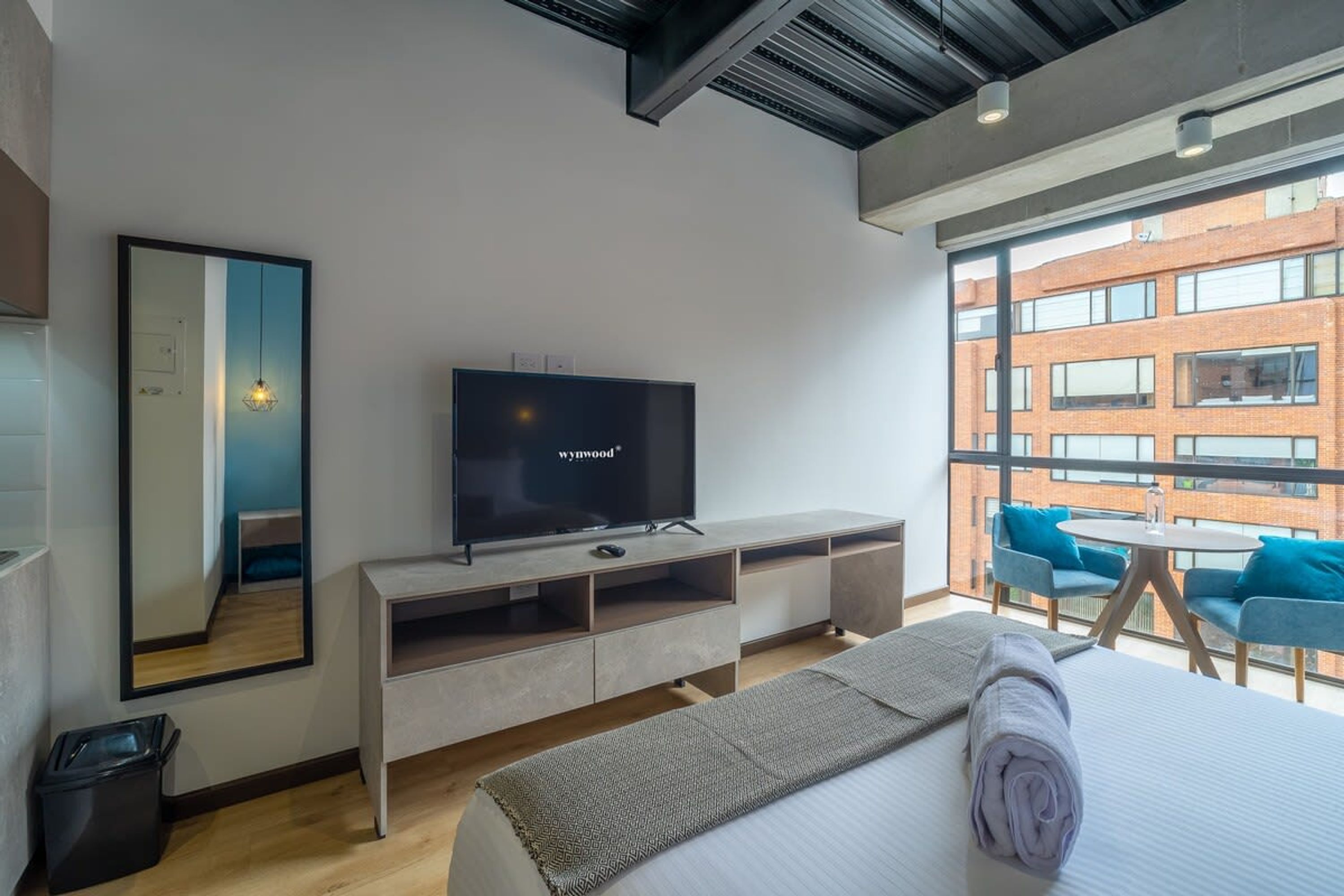 Habitació d'hotel moderna amb un llit gran, televisió, mirall i un balcó amb cadires blaves.