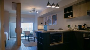 A modern kitchen with dark cabinetry, a central island, pendant lighting, and a view to a dining area. - w Great 1BR Apartment in Miraflores (Lima)