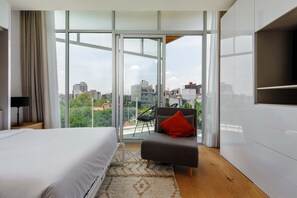 A modern hotel room with a large bed, a sofa with a red pillow, a chair, and a TV on a white cabinet. - w Fantastic Loft w/ Perfect View in Roma Norte (Mexico City)