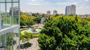 Un bâtiment moderne doté de grandes fenêtres donnant sur un parc avec une fontaine et des arbres.