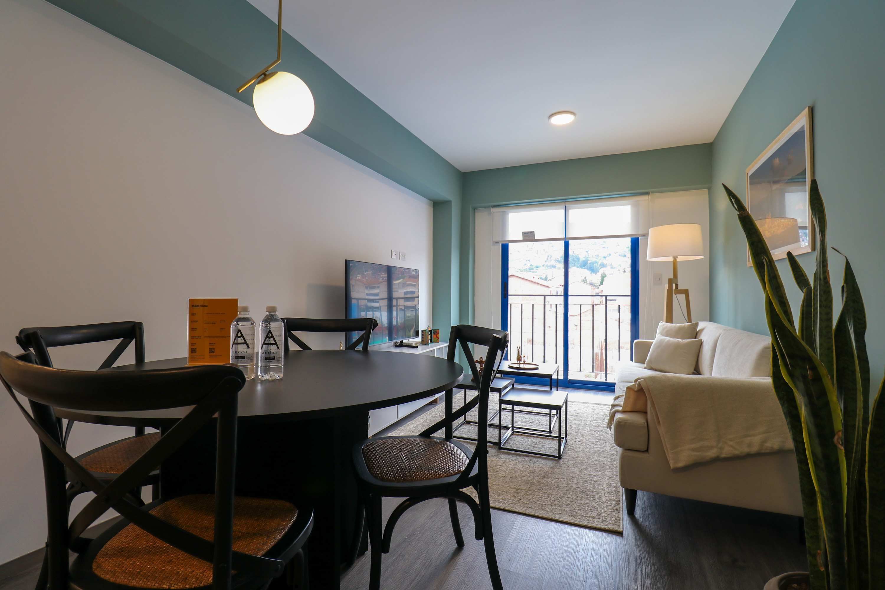 A modern living room with a dining area, a sofa, a coffee table, and a large window with a view.
