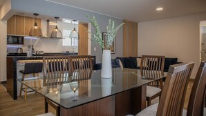 A modern kitchen with wooden cabinets, a microwave, and a coffee machine. There is a dining area with a glass table, chairs, and a vase with greenery. - w Stunning 3BR in Miraflores (Lima)