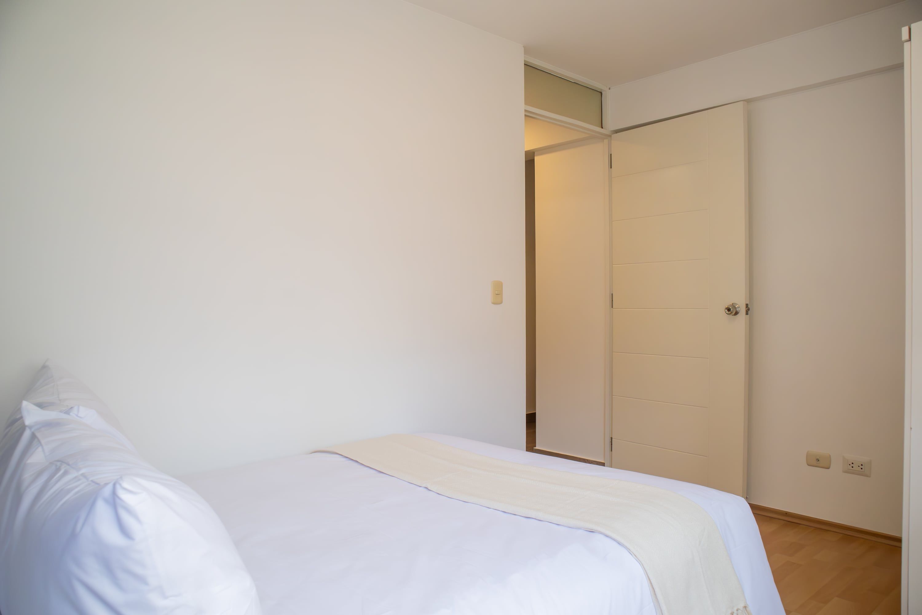 Une chambre à coucher avec un lit, un mur blanc, un plancher en bois et une armoire avec une porte coulissante.