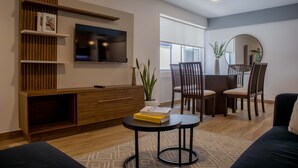 A modern living room with a TV, wooden shelving, a dining area with chairs, and a small round table. - w Stunning 3BR in Miraflores (Lima)