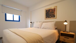 A neatly made bed with a beige blanket, a bedside table with a lamp, and a painting on the wall. - w Captivating 1BR w Perfect Terrace in Cusco (Cusco)