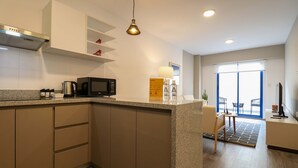 A modern kitchen with a central island, built-in cabinets, a microwave, and a kettle. There is a dining area with a table and chairs, and a large window providing natural light. - w Captivating 1BR w Perfect Terrace in Cusco (Cusco)
