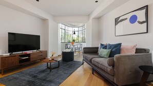 En moderne stue med et fladskærms-tv, en sofa med farverige puder, et sofabord og et spiseområde med bord og stole.