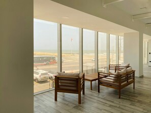 A spacious room with large windows offering a view of a beach and road. There are two wooden chairs and a small table.