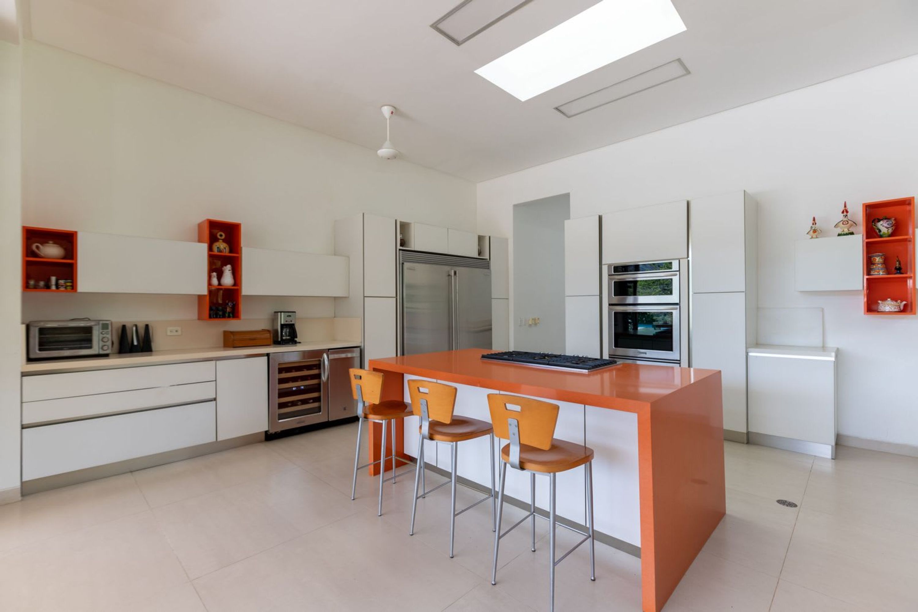 A modern kitchen with white cabinetry, a central island with bar stools, and built-in appliances.