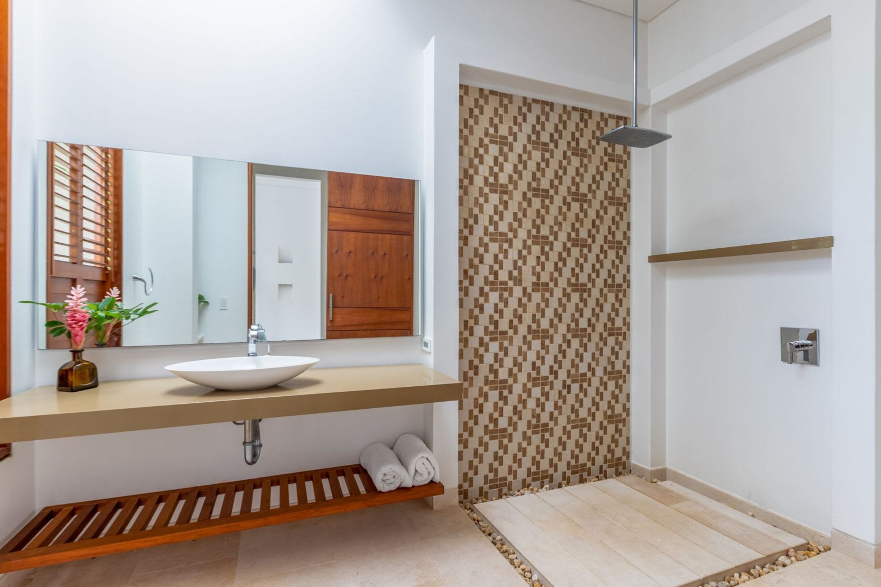 Un baño moderno con tocador de madera, un lavabo blanco, un espejo y zona de ducha con pared de baldosas estampadas.
