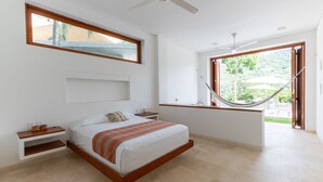 Un dormitorio con cama, mesita de noche, ventana, ventilador de techo y hamaca.