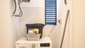 A compact laundry area with a front-loading washing machine, a water heater, and a window with blinds. - w Stunning 1BR w Great Deco in San Isidro (Lima)
