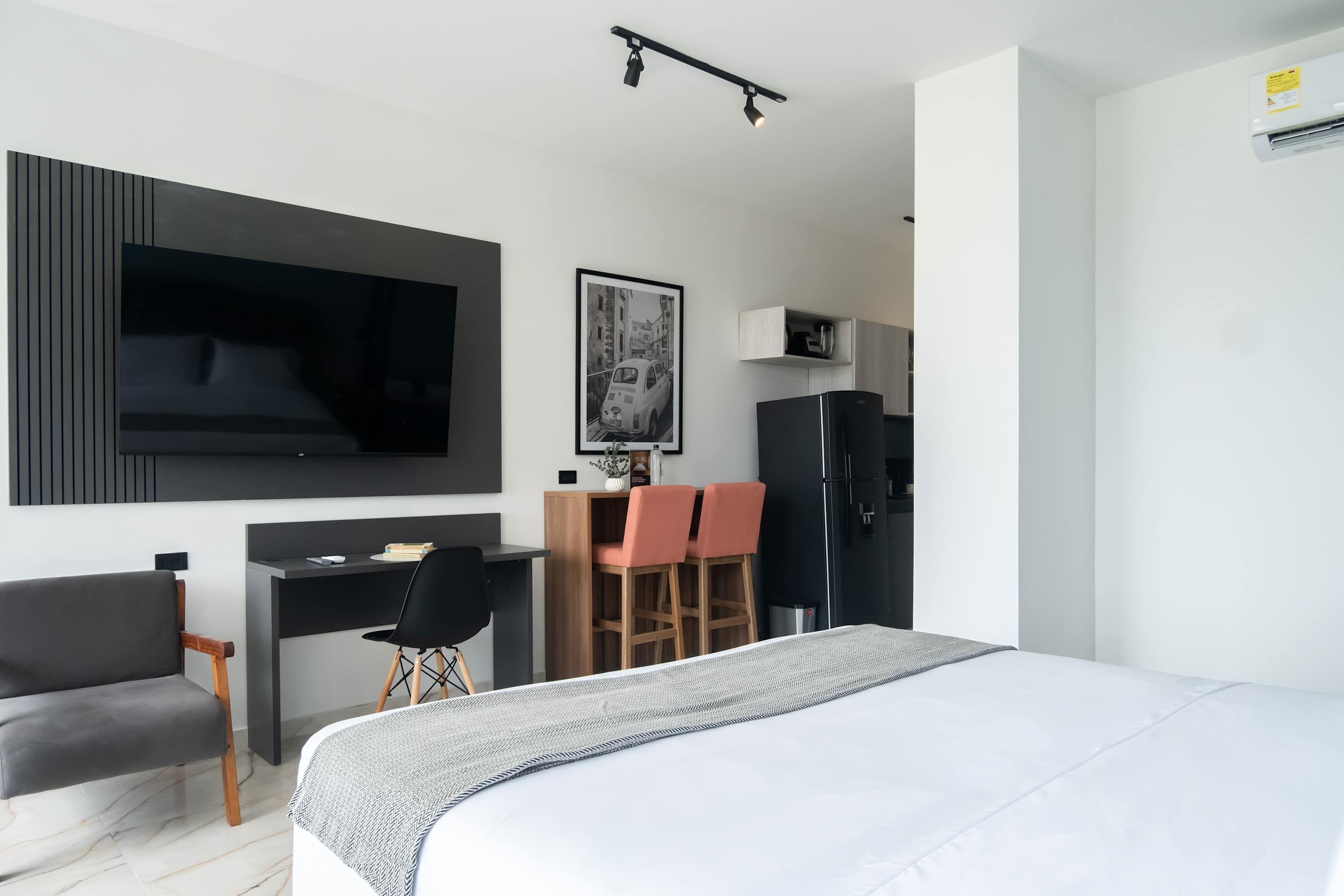 A modern hotel room with a large bed, a desk with two chairs, a television, and a refrigerator.