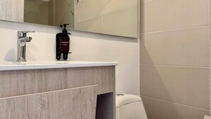 Un baño con tocador de madera, un espejo, un lavabo y un inodoro.