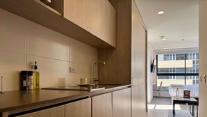 Una cocina moderna con armarios de madera, encimera de acero inoxidable y un lavabo integrado. Hay una botella de aceite y una taza sobre la encimera.