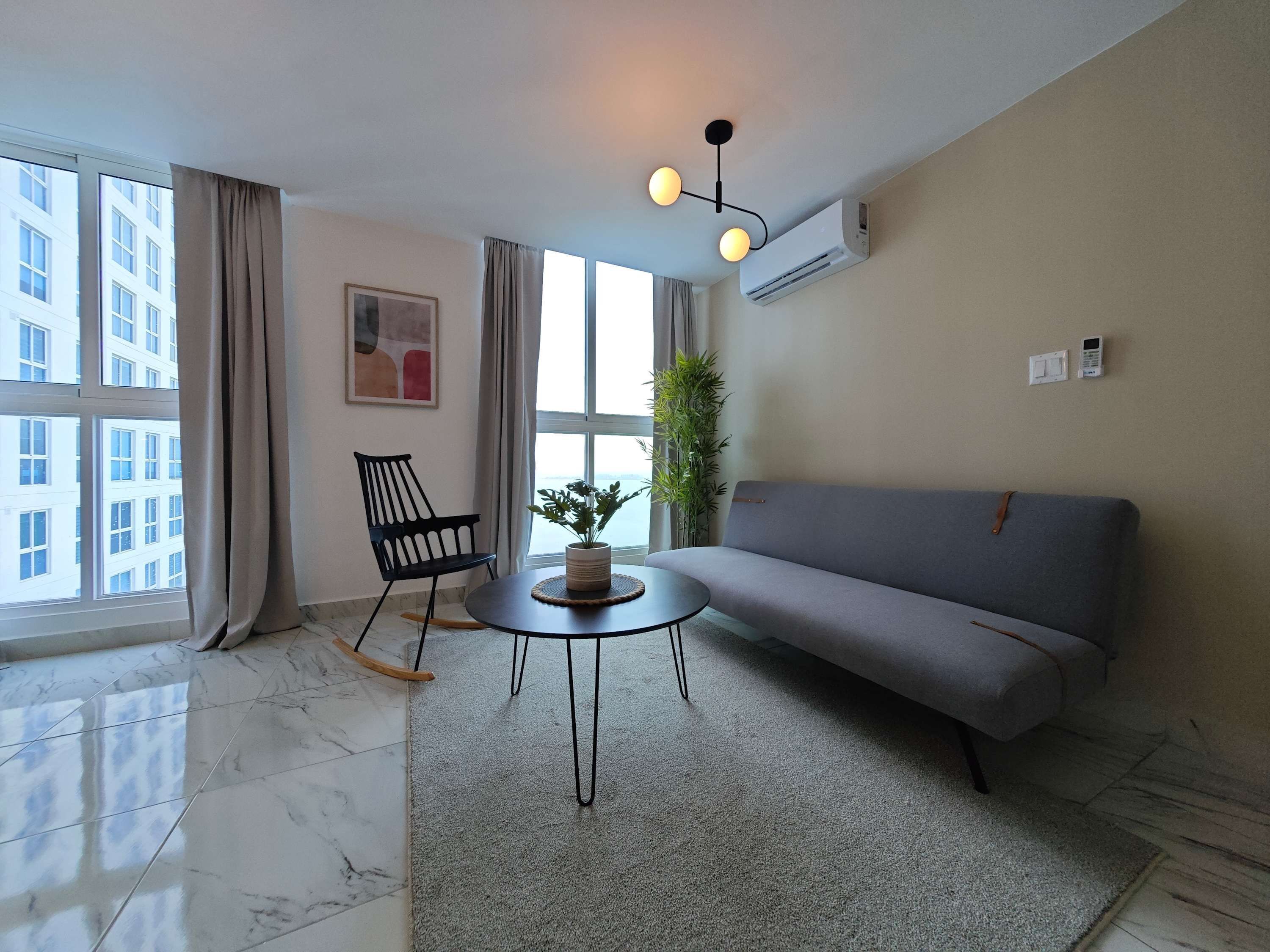 Un salon moderne avec un canapé gris, un fauteuil noir, une table basse ronde et une plante en pot.