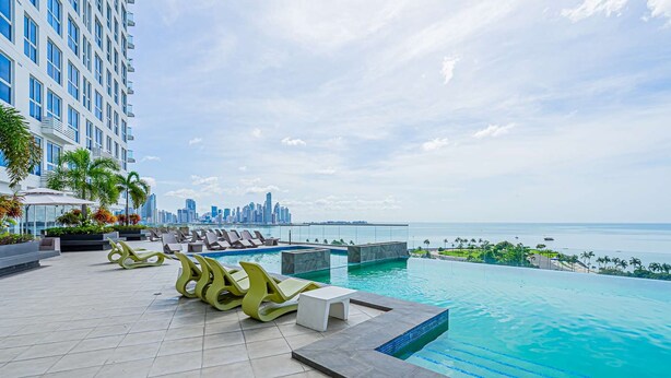A rooftop infinity pool with lounge chairs, a city skyline view, and a body of water in the background. - w Awesome 1BR w Great Deco in Avenida Balboa (Panama City)
