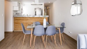 A modern kitchen with a wooden accent wall, a glass dining table with four chairs, and a built-in oven. - w Great 3BR Duplex With Terrace in Miraflores (Lima)