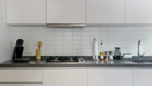 Cozinha moderna com armários brancos, fogão a gás, pia e diversos utensílios de cozinha.
