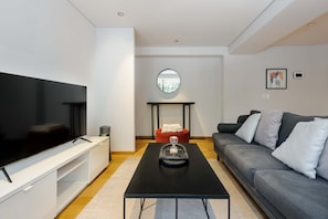 A modern living room with a flat-screen TV, a black coffee table, a grey sofa, and a red ottoman. - w Radiant 2BR in Roma Norte (Mexico City)