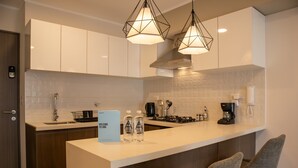 Une cuisine moderne avec des meubles blancs, un îlot central, des tabourets de bar et des luminaires suspendus aux formes géométriques.