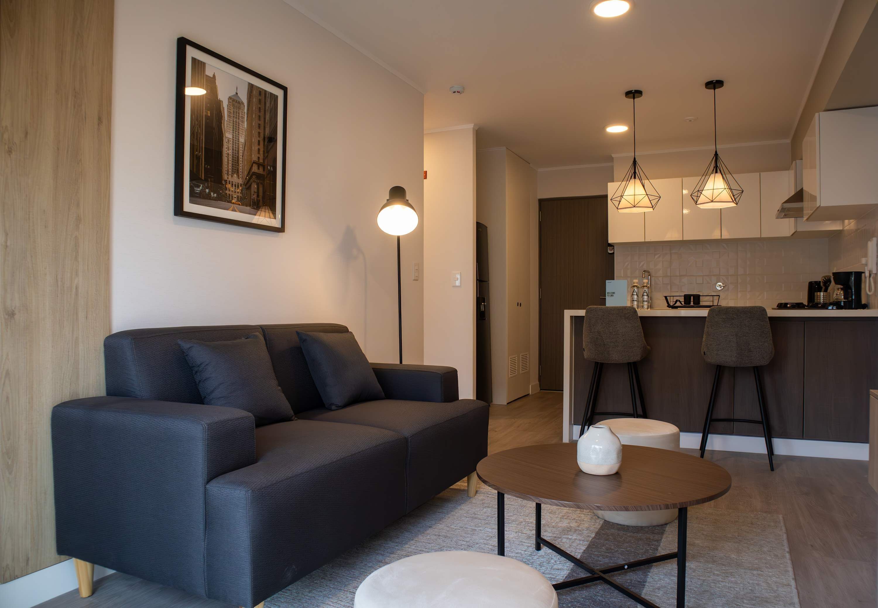 A modern living room with a sofa, a coffee table, and a kitchen area with bar stools.