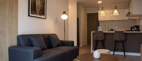 A modern living room with a sofa, a coffee table, and a kitchen area with bar stools.