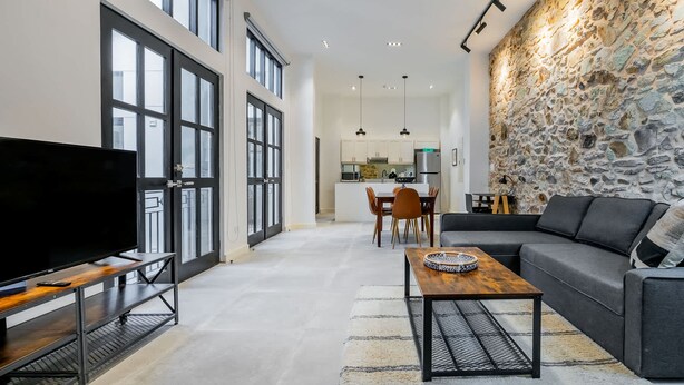 A modern living room with a TV, sofa, and coffee table. There is a stone wall and a kitchen in the background. - w Contemporary 1BR in Plaza Catedral (Panama City)