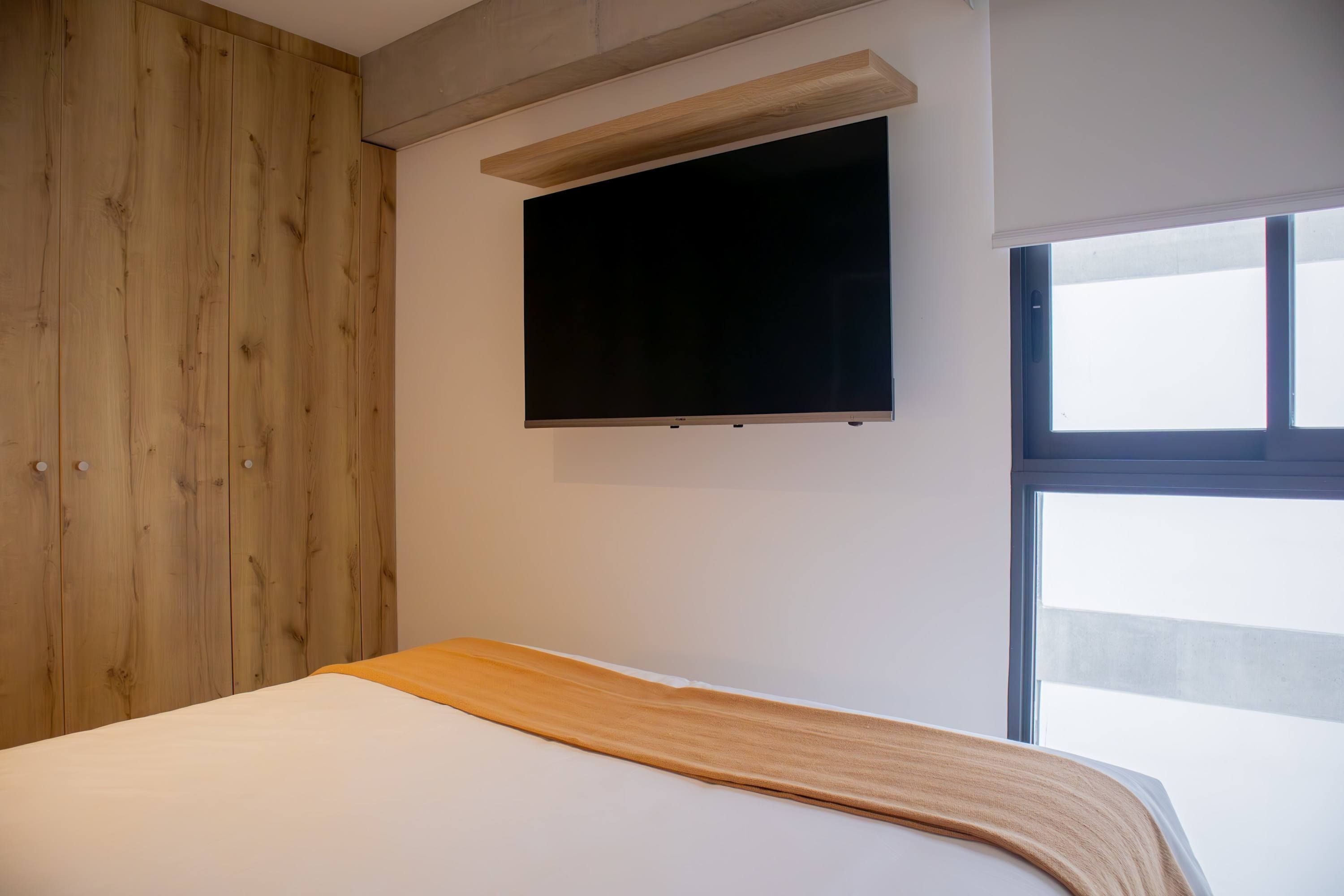 Een slaapkamer met een bed, een houten garderobe, een bevestigde televisie en een raam.