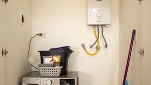 Ett utrymme för tvätt med en tvättmaskin, en tvättkorg, en mopp och en varmvattenberedare.