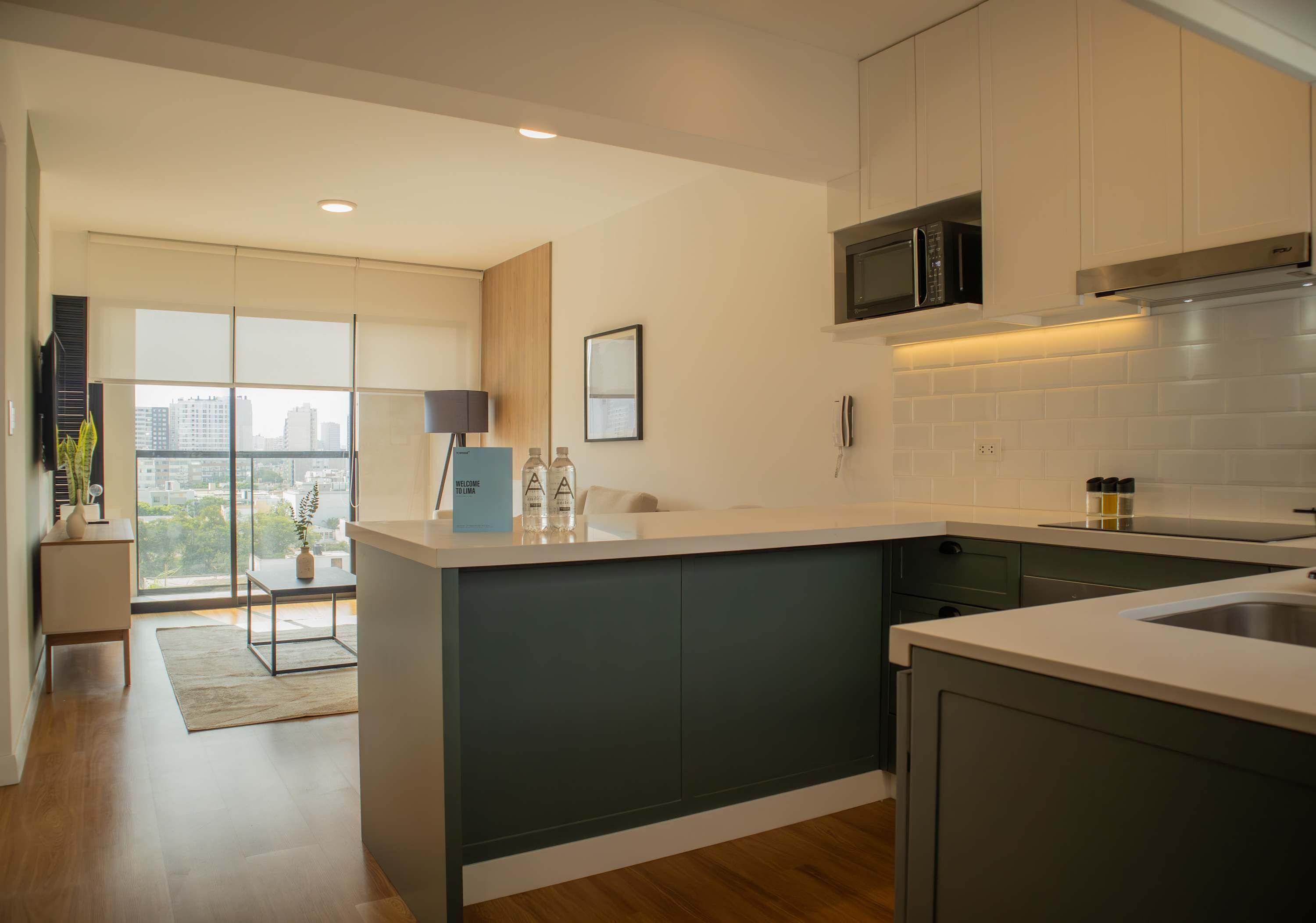 A modern kitchen with a central island, dark cabinetry, and a view of the city through large windows.