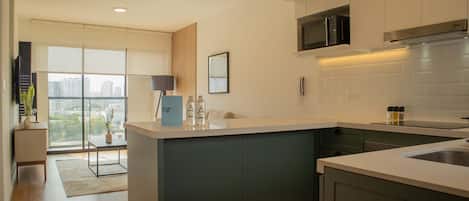 A modern kitchen with a central island, dark cabinetry, and a view of the city through large windows.