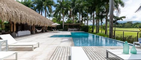 A pool area with lounge chairs and a thatched-roof structure.