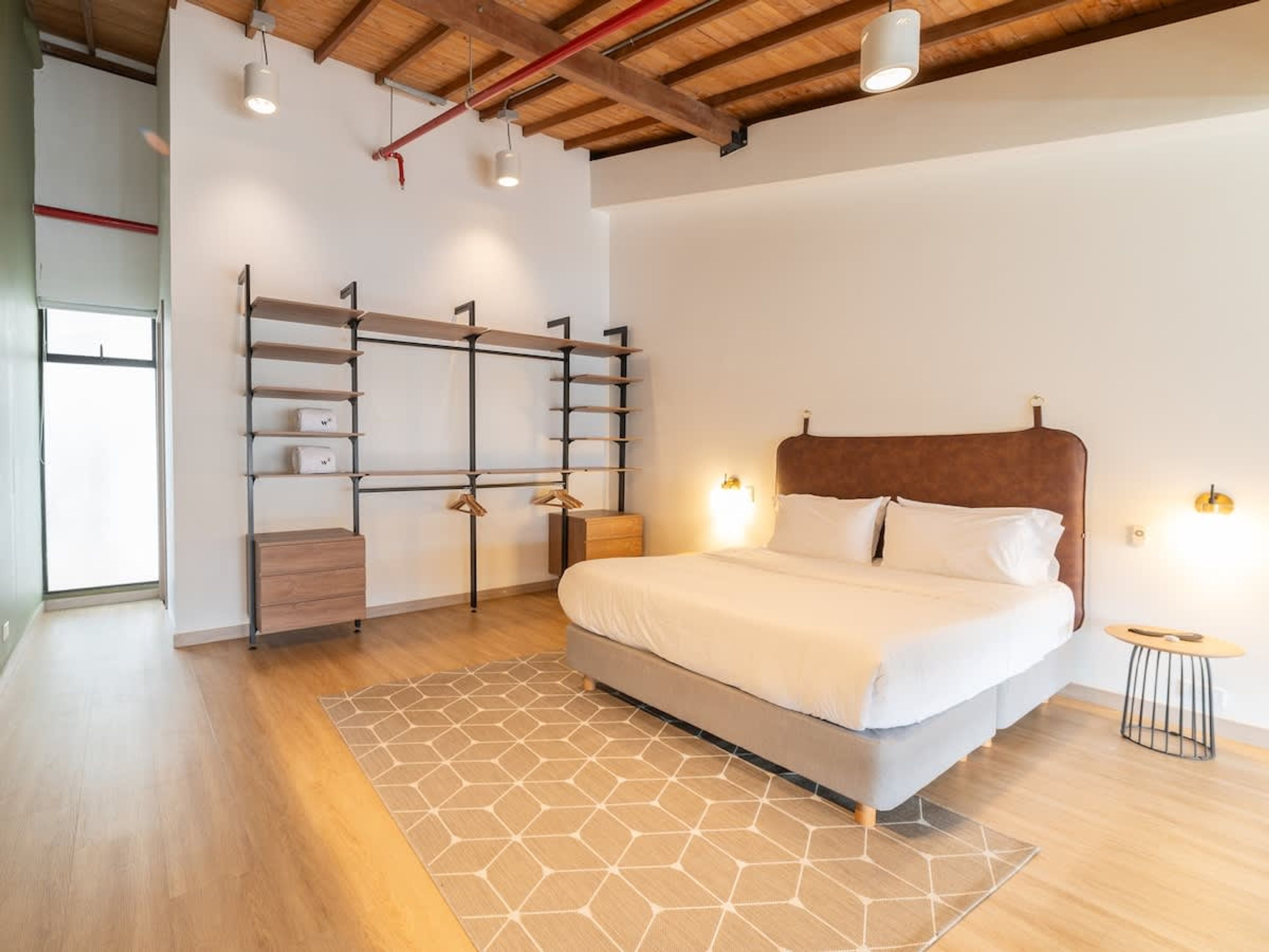 A modern bedroom with a large bed, built-in shelving, and a geometric-patterned rug.