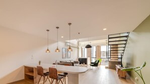 A modern kitchen with a central island, dining area with chairs, and a staircase leading to an upper level. - w Stylish Duplex in Laureles (Medellín)