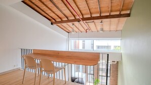 A spacious room with a high ceiling, wooden beams, a large window, and a dining area with a table and chairs. - w Stylish Duplex in Laureles (Medellín)