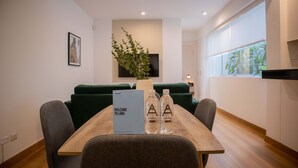 A modern dining area with a wooden table, two grey chairs, a green sofa, a potted plant, and a welcome sign. - w Striking 1BR in Miraflores (Lima)