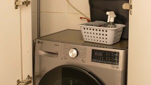 A compact laundry room with a washing machine and a water heater, featuring a control panel and a basket on the machine. - w Striking 1BR in Miraflores (Lima)