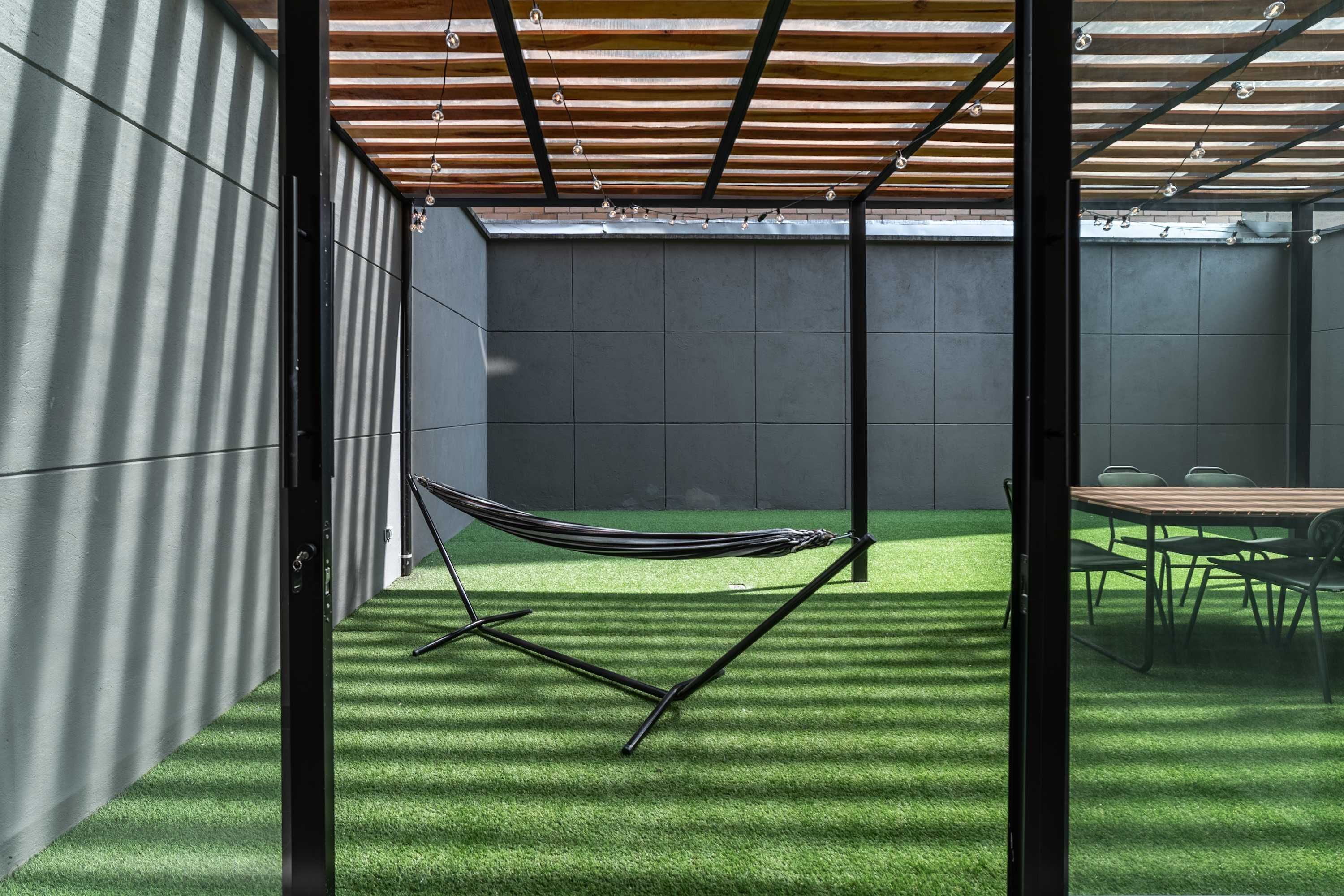 Moderni ulkotila, jossa on riippumatto, pöytä ja tuolit sekä pergola.